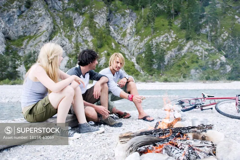 Germany, Bavaria, Tölzer Land, Young people sitting at campfire near river