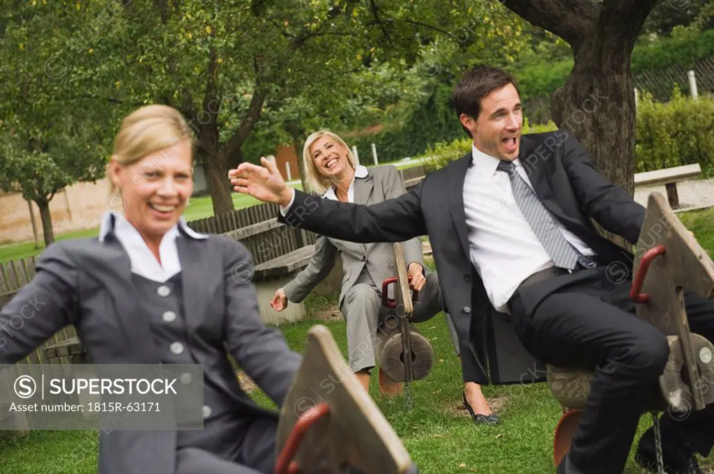 Germany, business people riding rocking horses in playground