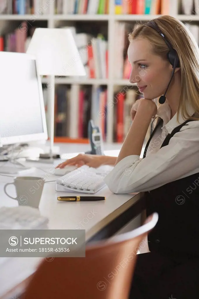 Young woman in office with headset using computer, portrait