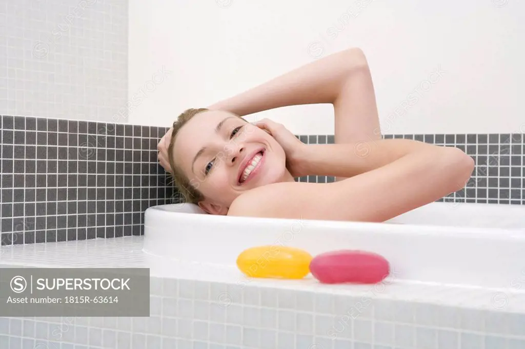 Young woman taking bath, smiling, side view, portrait