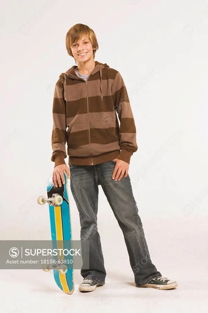 Teenage boy 13_14 standing with skateboard over head, smiling