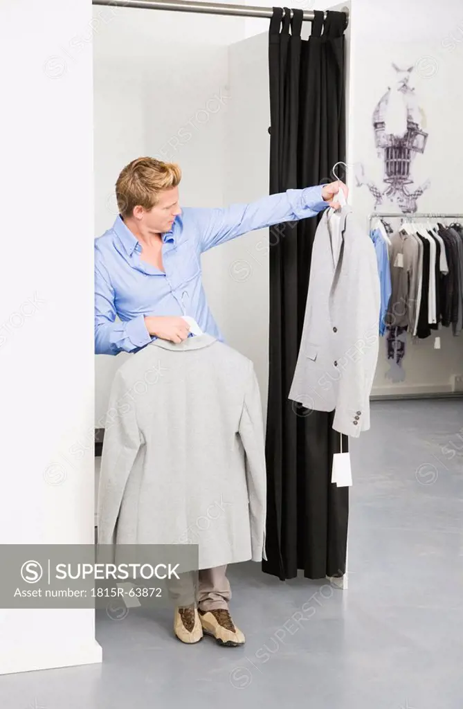 Young man in changing room, holding jackets
