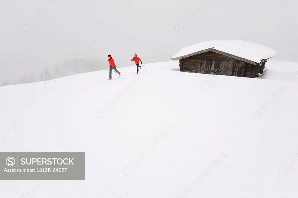 Italy, South Tyrol, Couple cross_country skiing next to cabin