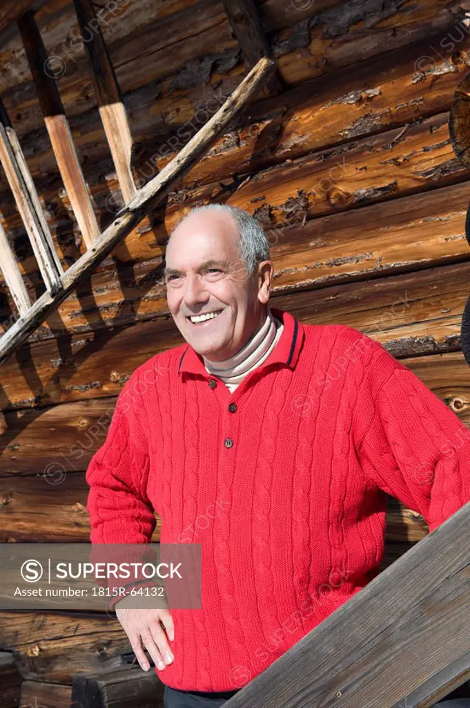 Italy, South Tyrol, Seiseralm, Senior man standing in front of wooden wall, smiling, portrait