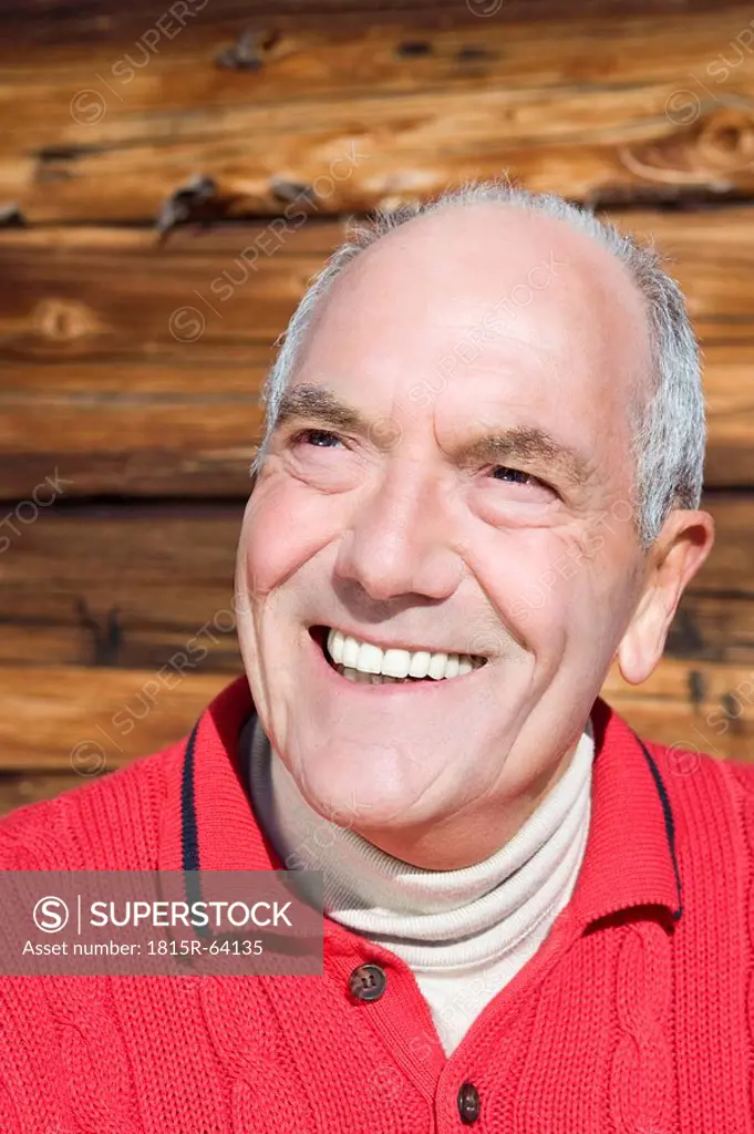 Italy, South Tyrol, Seiseralm, Senior man in front of wooden wall, smiling, close_up
