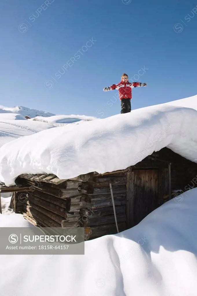 Italy, South Tyrol, Seiseralm, Boy 4_5 standing on snow_covered roof of log cabin