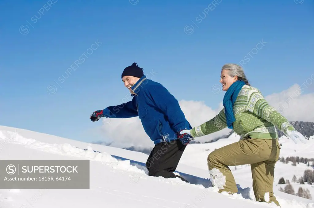 Italy, South Tyrol, Seiseralm, Senior couple walking in snow, side view, portrait