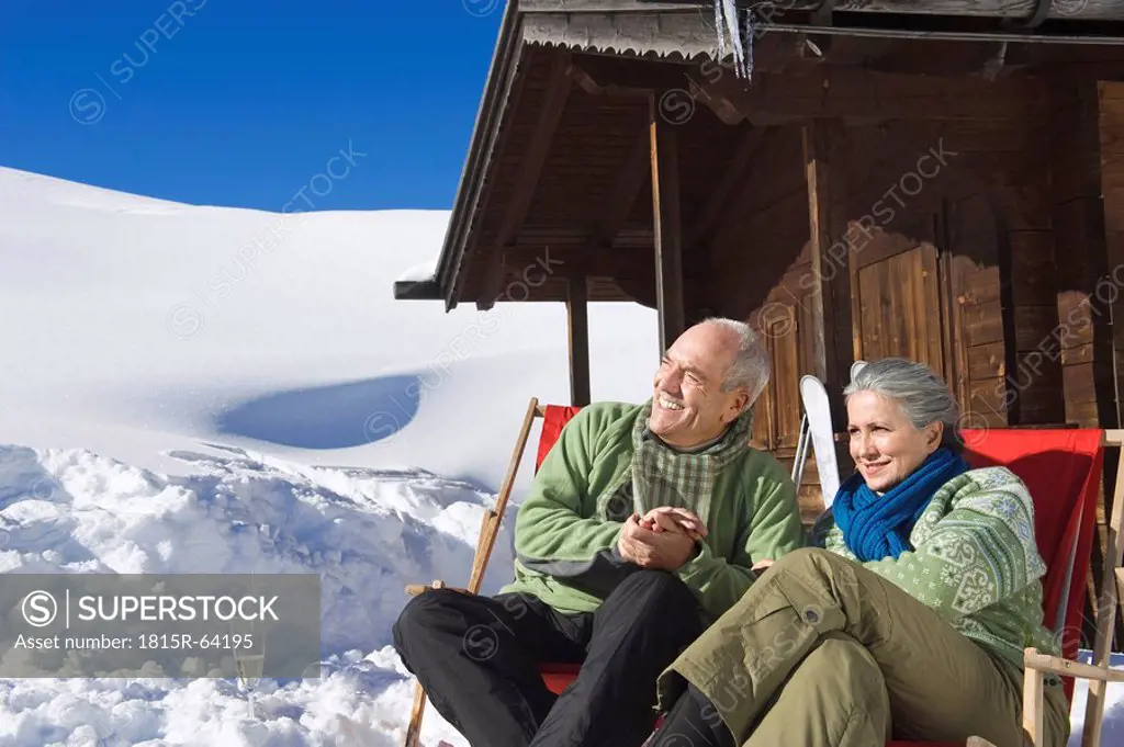 Italy, South Tyrol, Seiseralm, Senior couple sitting in front of log cabin, smiling, portrait