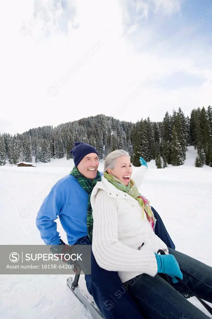 Italy, South Tyrol, Seiseralm, Senior couple sledding down hill, laughing, portrait