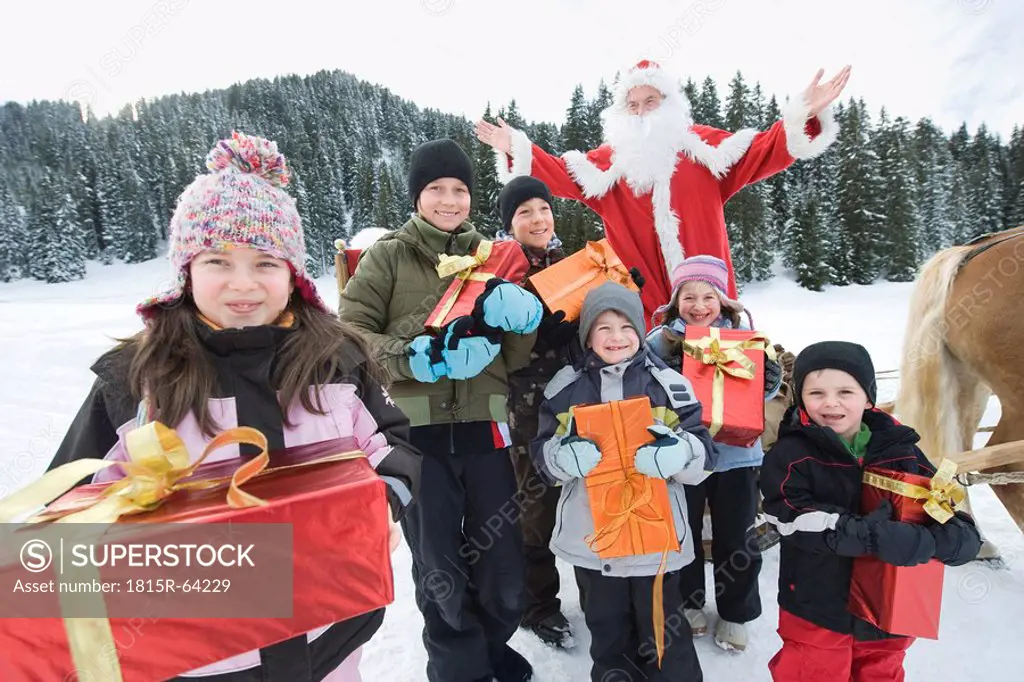 Italy, South Tyrol, Seiseralm, Children holding gift parcels, Santa Claus in background, portrait