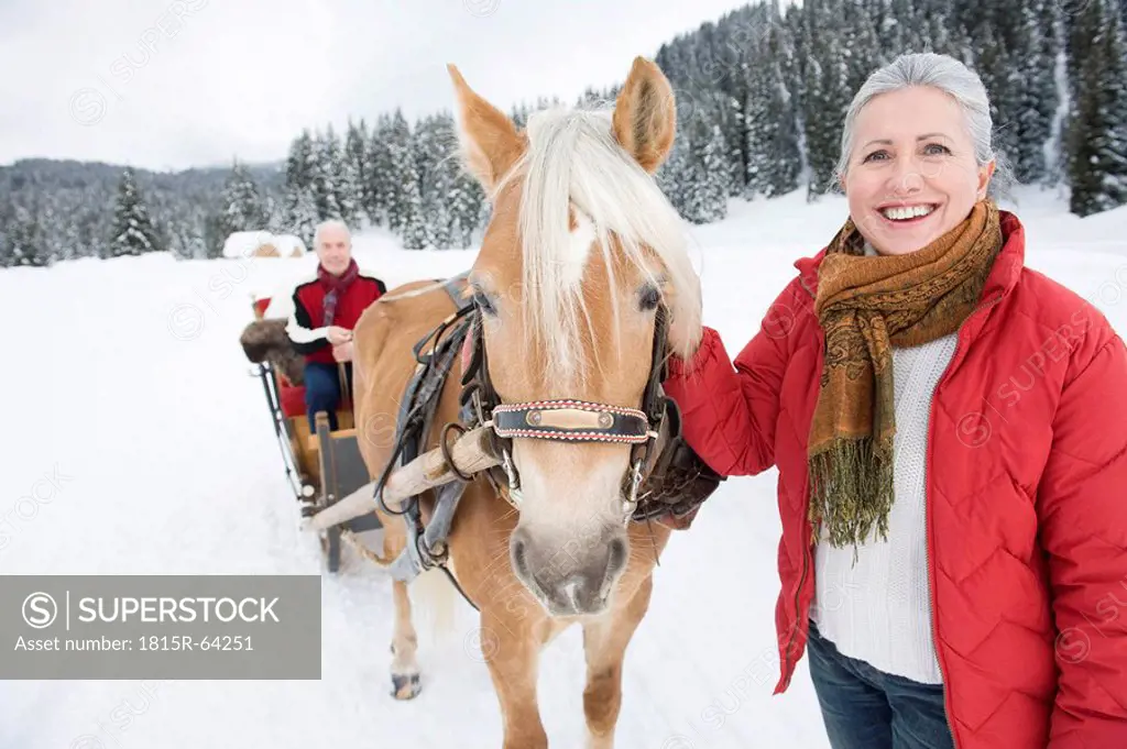 Italy, South Tyrol, Seiseralm, Senior woman standing by horse, man sitting in sleigh, smiling, portrait