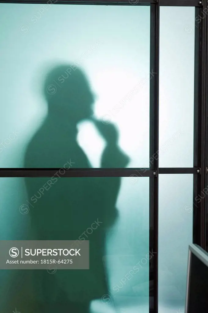 Germany, Munich, Silhouette of businessman behind frosted glass, hand to chin