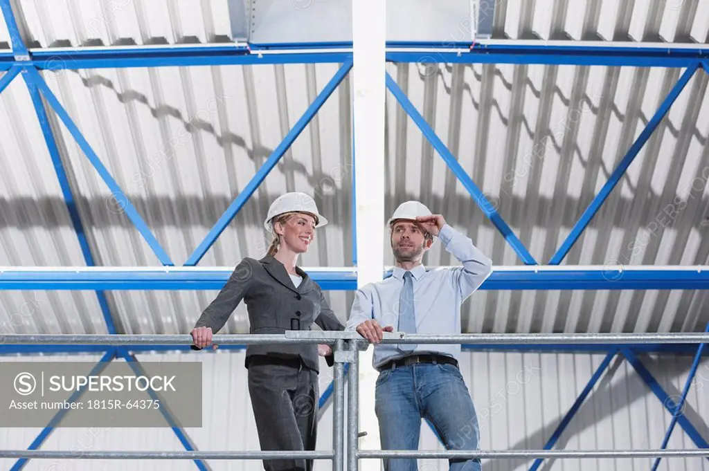 Germany, Neukirch, Man and woman architect standing in industrial hall, low angle view