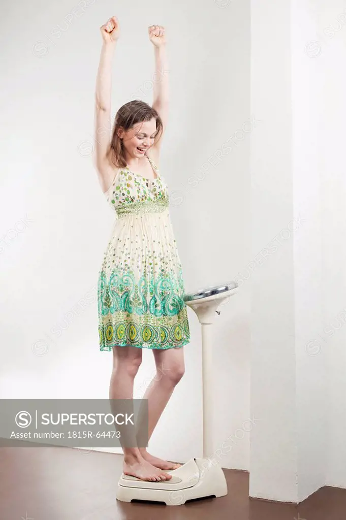 Germany, Bavaria, Munich, Young woman standing on scale, cheering