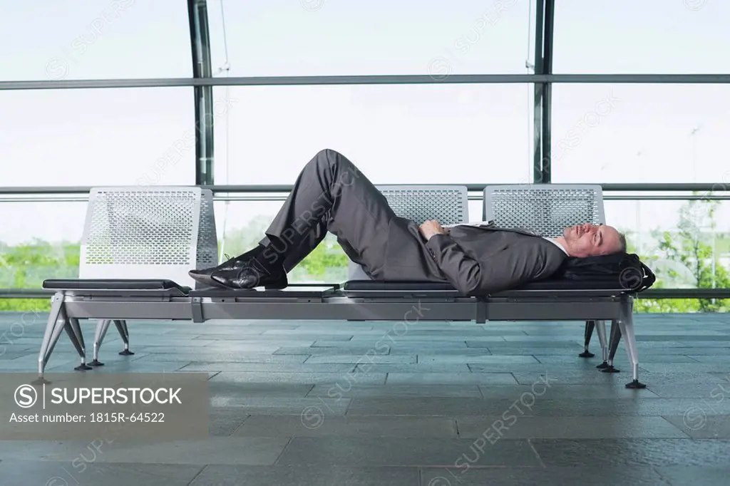 Germany, Leipzig_Halle, Businessman in Airport departure lounge, sleeping on bench