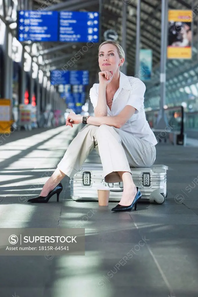 Germany, Leipzig_Halle, Young woman in Airport departure lounge, sitting on suitcase