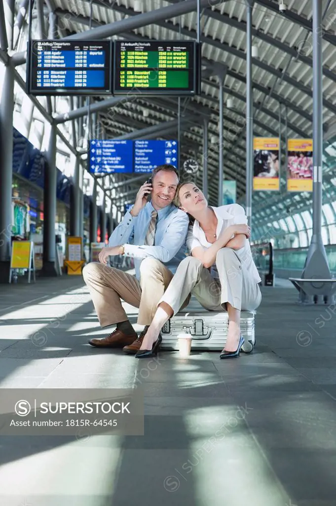 Germany, Leipzig_Halle, Airport, Businessman and businesswoman sitting on suitcase