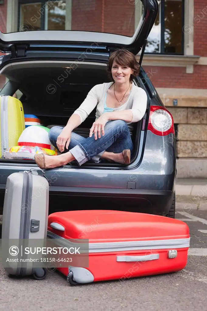 Germany, Leipzig, Woman sitting at back of car, suitcase in foreground