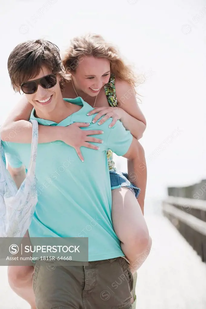 Germany, Bavaria, Ammersee, Young man giving young woman a piggy back on jetty, portrait