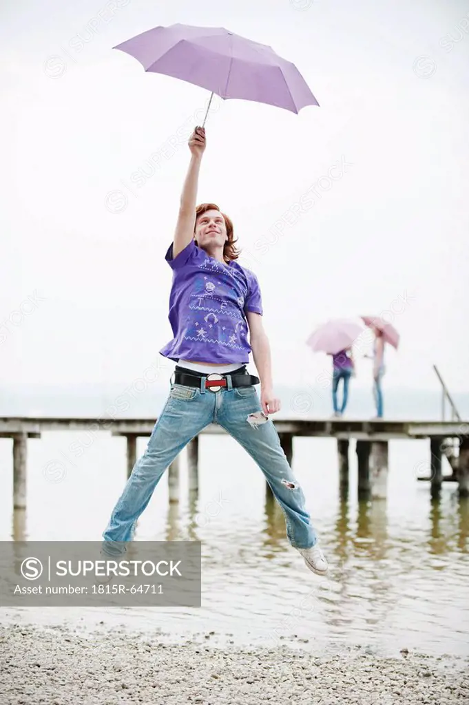 Germany, Bavaria, Ammersee, Young man holding umbrella and jumping