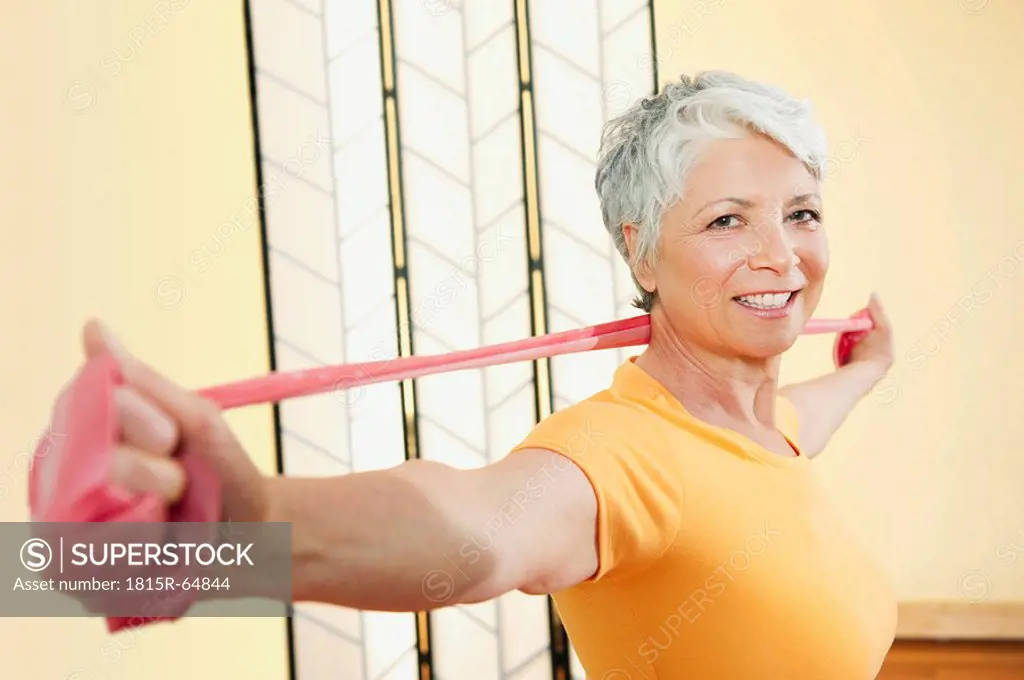 Senior woman exercising with elastic band, smiling, portrait