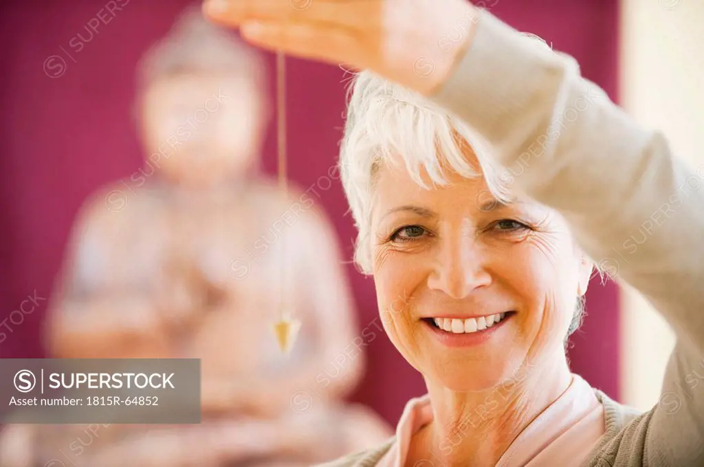 Senior woman holding pendulum, smiling, portrait