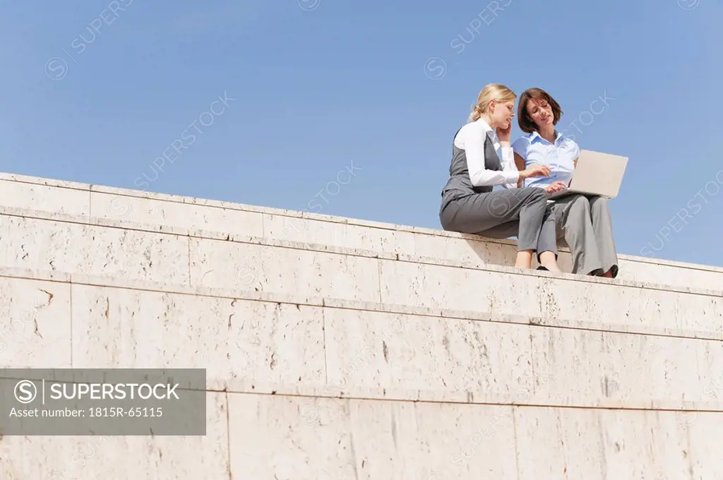 Spain, Mallorca, Two Businesswomen sitting on stairs using laptop