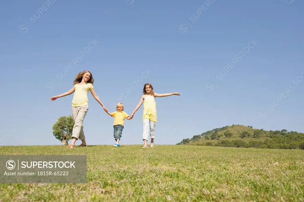 Spain, Mallorca, Mother and children 4_5, 10_11, walking across meadow