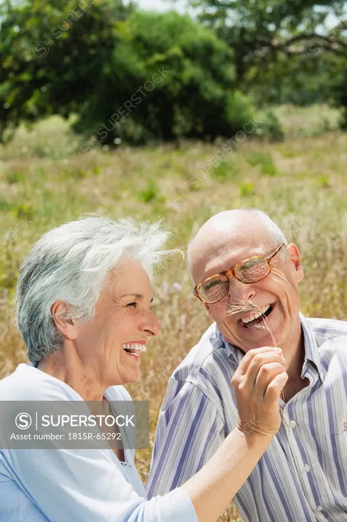 Spain, Mallorca, Senior couple sitting on grass, having fun, portrait