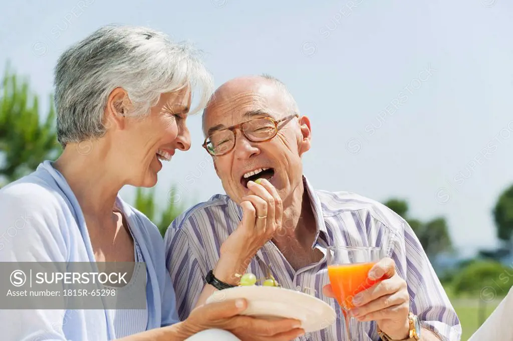 Spain, Mallorca, Senior woman feeding grapes to senior man, laughing, portrait