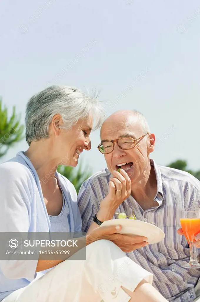 Spain, Mallorca, Senior woman feeding grapes to senior man, laughing, portrait