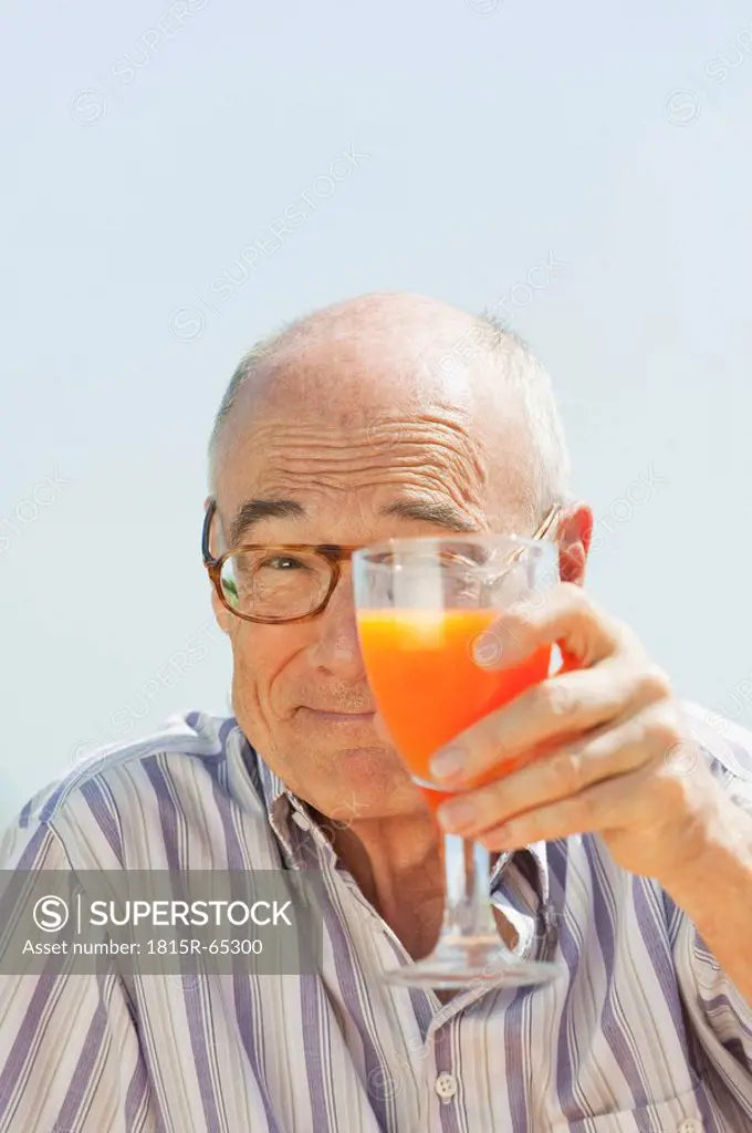 Spain, Mallorca, Senior man holding glass with orange juice, portrait