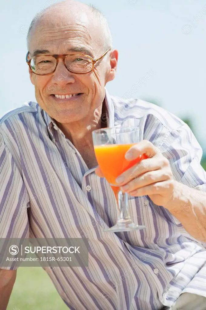 Spain, Mallorca, Senior man holding glass with orange juice, portrait