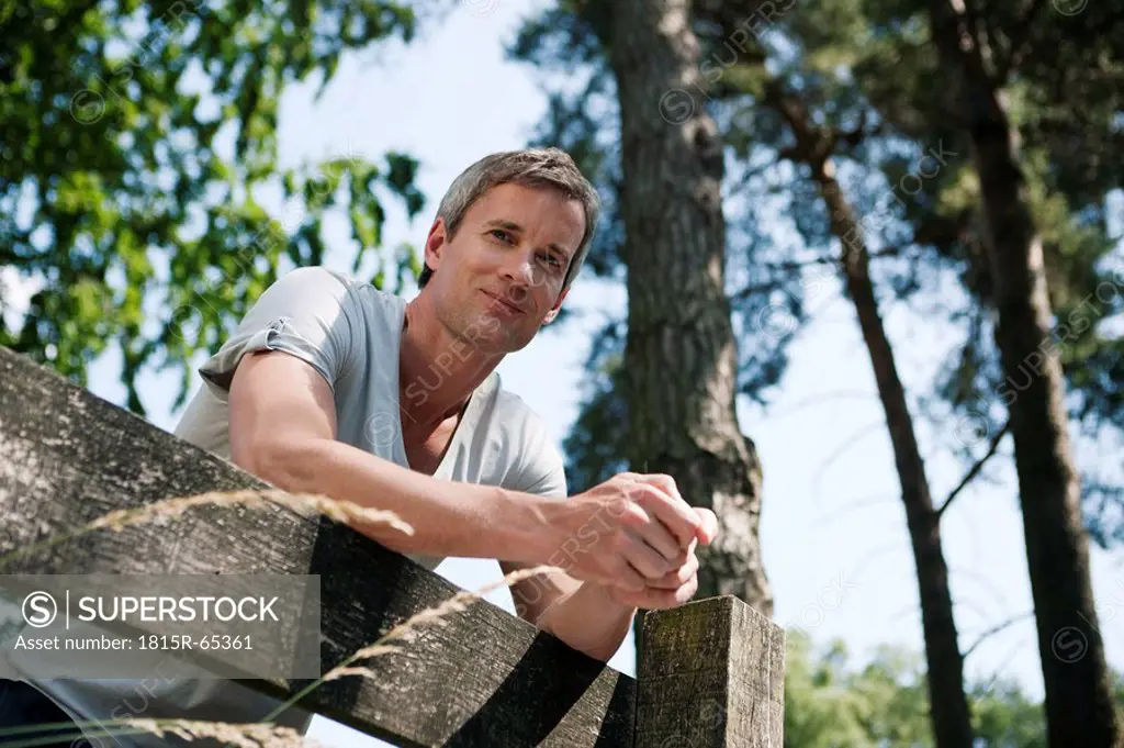 Germany, Hamburg, Man leaning against wooden fence, low angle view