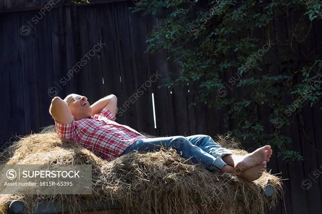 Germany, Bavaria, Senior man lying on haystack