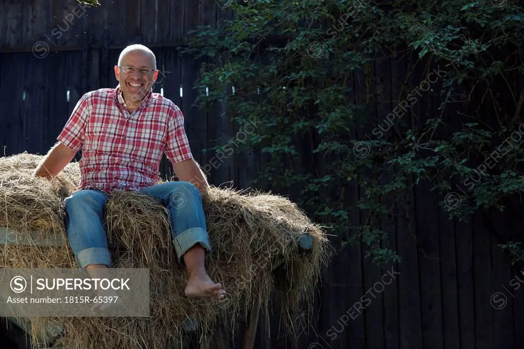 Germany, Bavaria, Senior man sitting on haystack
