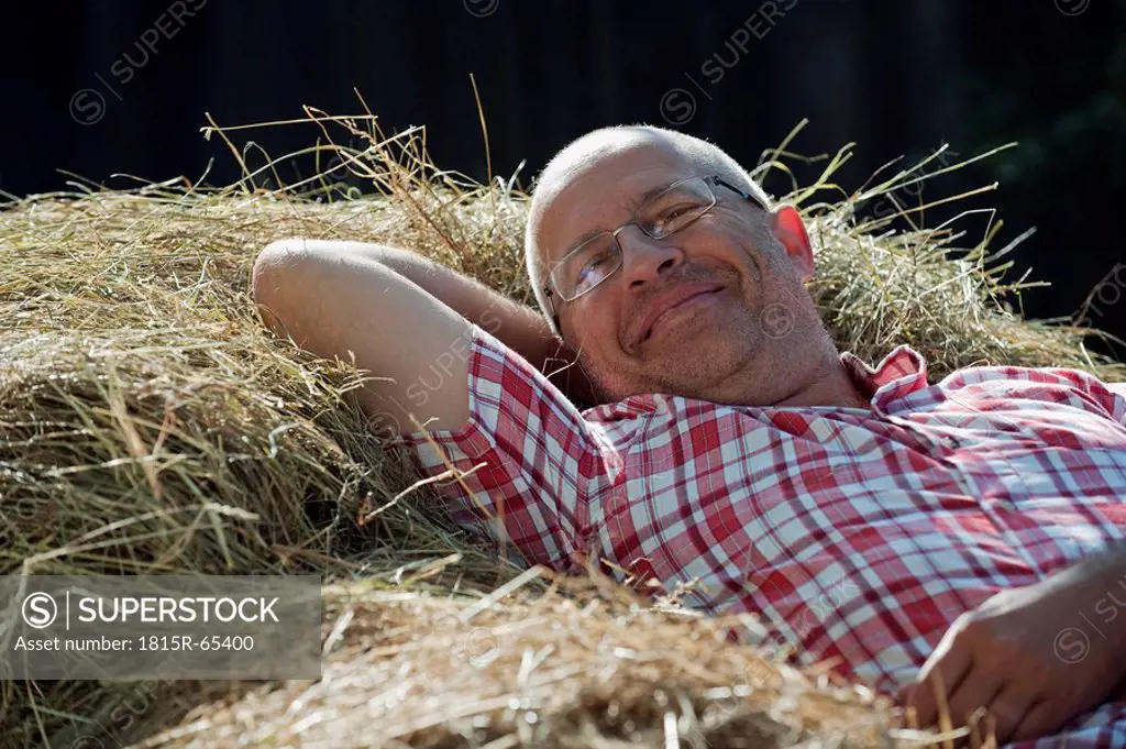 Germany, Bavaria, Senior man lying on haystack