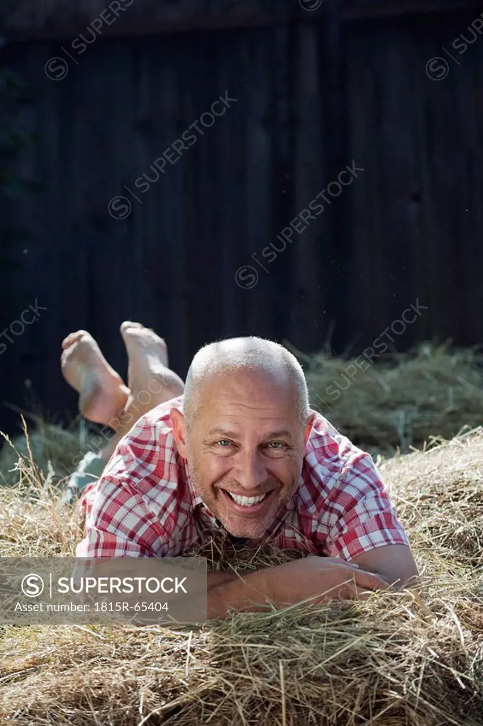 Germany, Bavaria, Senior man lying on haystack, smiling, portrait