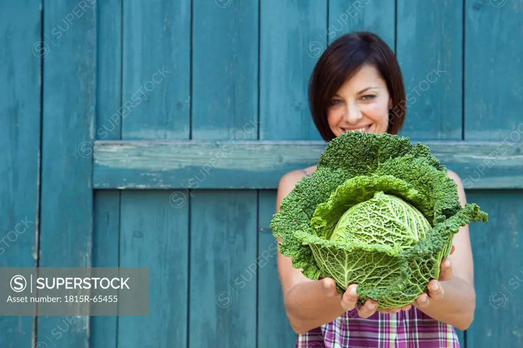 Germany, Bavaria, Woman holding savoy cabbage, smiling, portrait