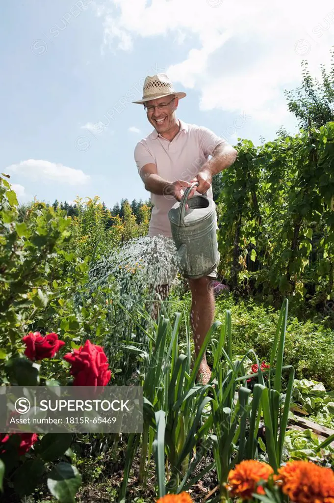 Germany, Bavaria, Senior man watering flowers, laughing, portrait