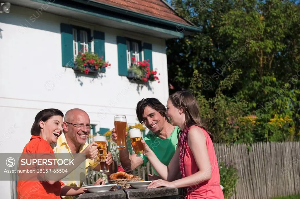 Germany, Bavaria, Four persons drinking beer in the garden, having fun, portrait