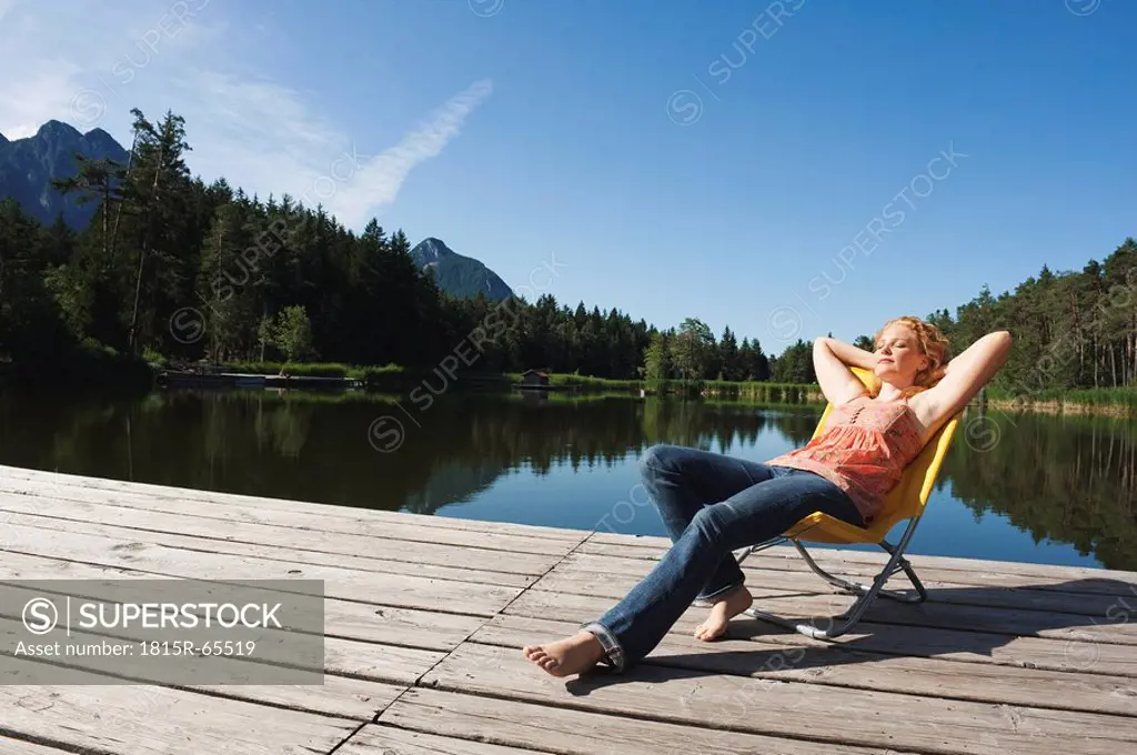 Italy, South Tyrol, Woman sunbathing on jetty by lake