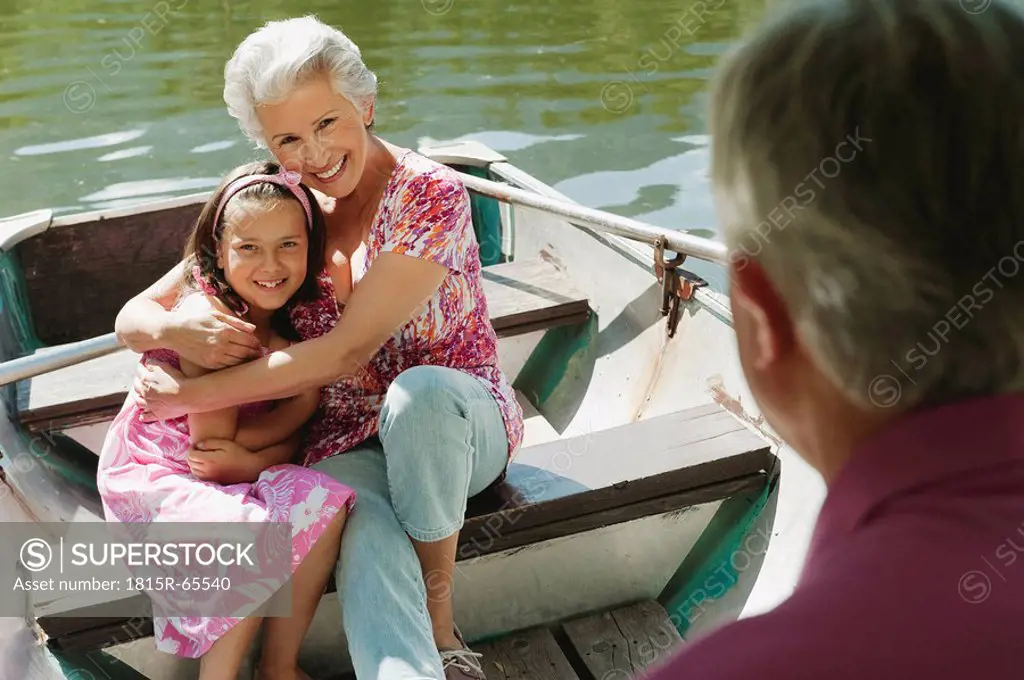 Italy, South Tyrol, Grandparents and granddaughter 8_9 sitting in rowing boat, smiling, portrait