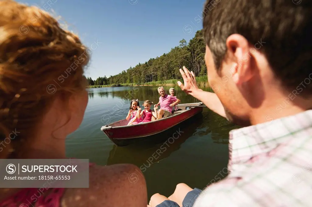 Italy, South Tyrol, Grandparents and grandchildren in rowing boat, parents waiting on jetty