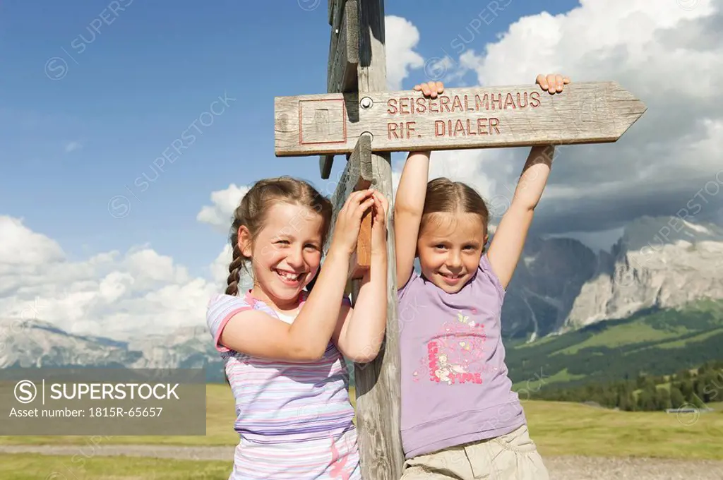 Italy, Seiseralm, Girls 6_7, 8_9 standing by sign post, smiling, portrait