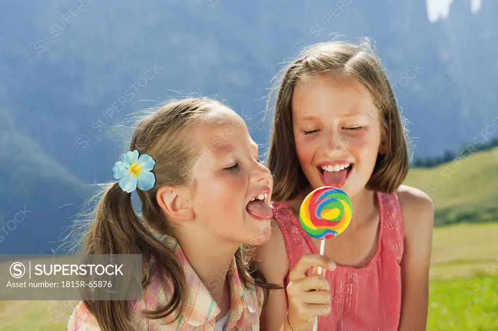 Italy, South Tyrol, Two girls 6_7 10_11 licking lollypop, portrait, close_up