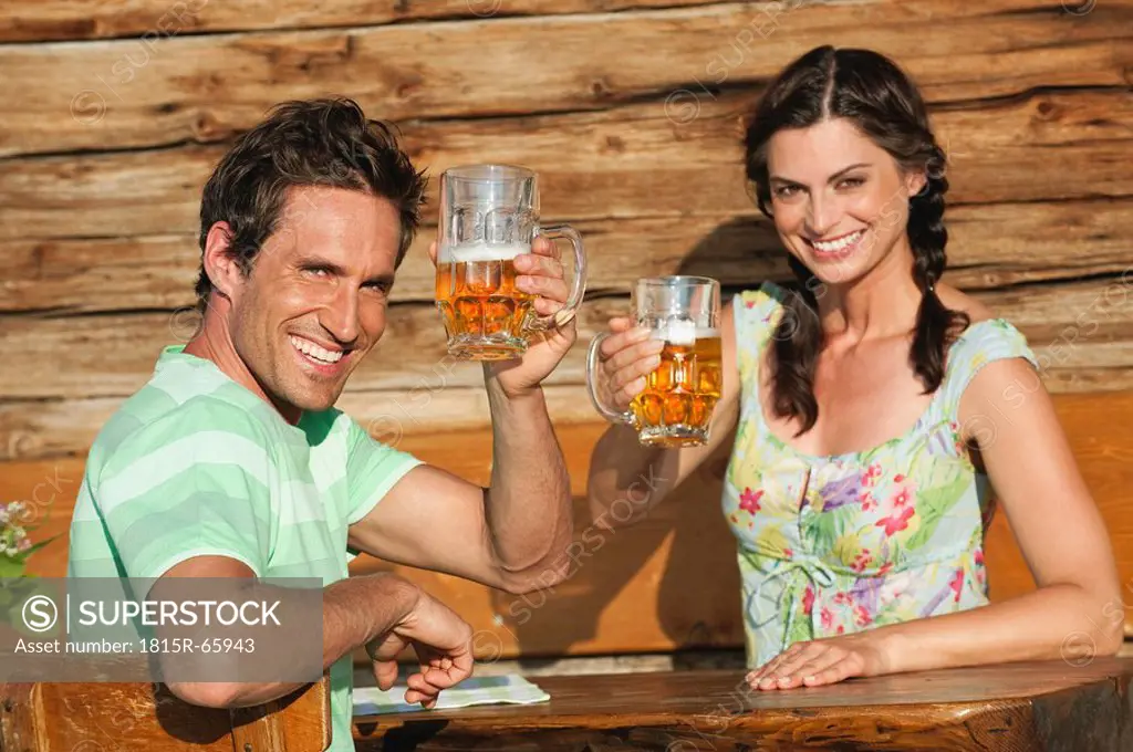 Italy, South Tyrol, Couple holding beer mugs, smiling, portrait