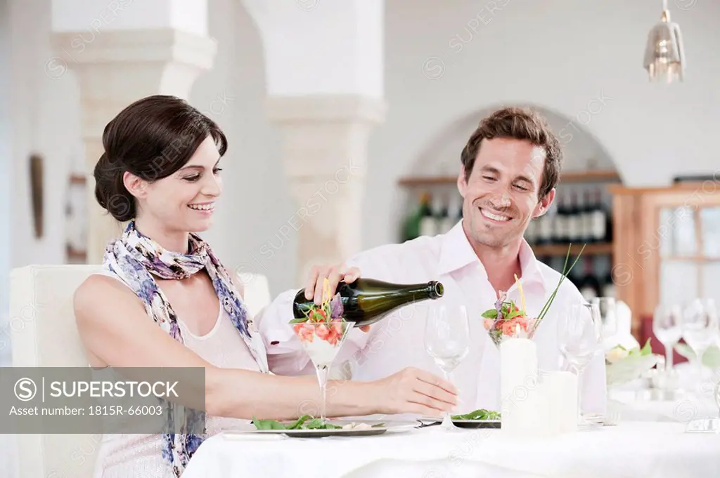 Couple in restaurant, man pouring wine into glass, smiling, portrait