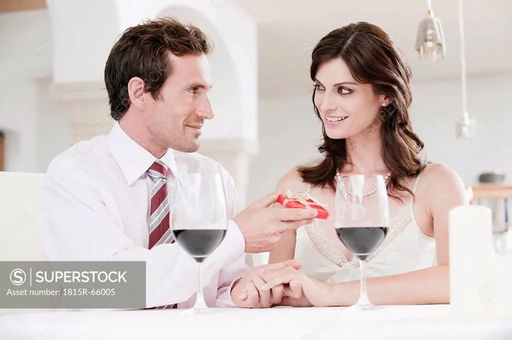 Couple sitting at table in restaurant, man holding gift parcel