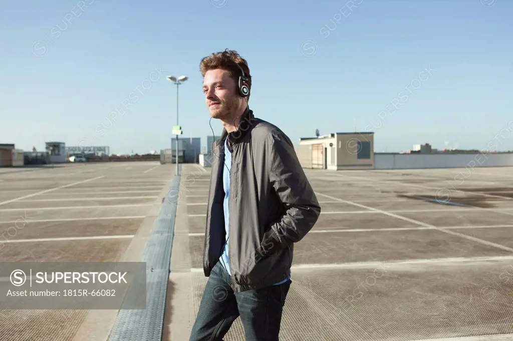 Germany, Berlin, Young man standing in car park listening to headphones
